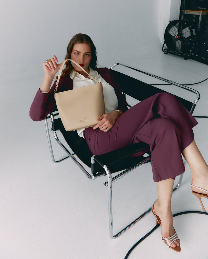 Imagen de modelo sentada con bolso de hombro tipo tote bag de piel beige multiposición Leandra. Bolso made in Spain. 